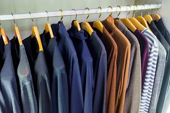 Wardrobe with jumpers and pullovers hanging on hangers in closet.